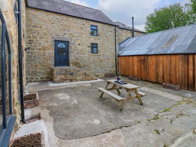 A stone courtyard with a wooden picnic table and planter boxes at The Coach House in Great Whittington near Corbridge