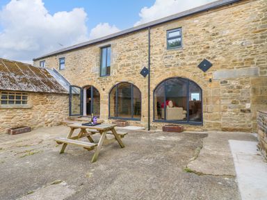 A stone house with arched windows and a wooden picnic table outside at The Coach House in Great Whittington near Corbridge