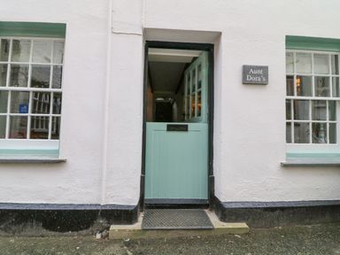 The exterior of a building with a half-open mint green door and two windows with white frames at Aunt Dora's in Port Isaac