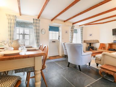 A dining area with wooden table and chairs and a living area with armchairs coffee table wood stove and wooden shelves at Aunt Dora's in Port Isaac