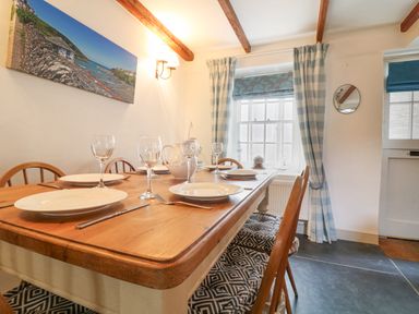 A dining room with a wooden table set with plates and glasses by a window with blue check curtains at Aunt Dora's in Port Isaac