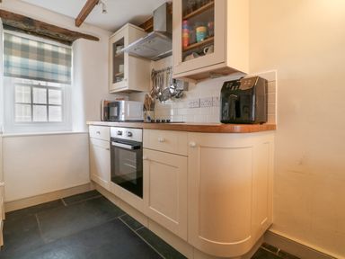 A kitchen with white cabinets a wooden countertop an oven a microwave and a black appliance on the counter at Aunt Doras in Port Isaac
