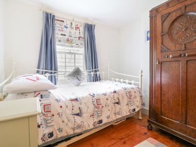 A bedroom with a single bed near a window with blue curtains and a wooden wardrobe at Aunt Dora's in Port Isaac