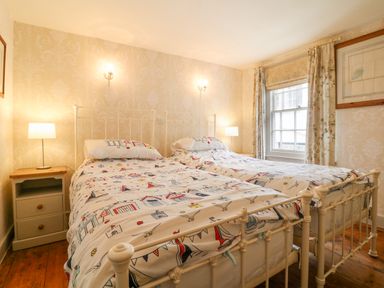 A bedroom with two single beds with patterned bedding bedside tables with lamps and a window with curtains at Aunt Dora's in Port Isaac
