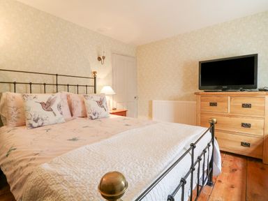 A bedroom with a metal bed frame a wooden dresser with a TV and floral bedding at Aunt Dora's in Port Isaac