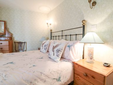 A bedroom with a double bed with bird patterned bedding bedside tables with lamps a wooden chair and a dresser with a mirror at Aunt Dora's in Port Isaac