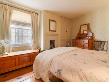 A bedroom with a bed a wooden dresser a chair and a window with curtains at Aunt Dora's in Port Isaac