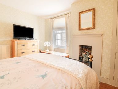 A bedroom with a bed a wooden dresser a window with curtains and a fireplace at Aunt Dora's in Port Isaac