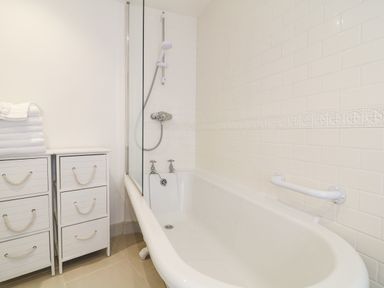 A bathroom with a white bathtub a shower head towels on a cabinet and white tiled walls at Aunt Dora's in Port Isaac