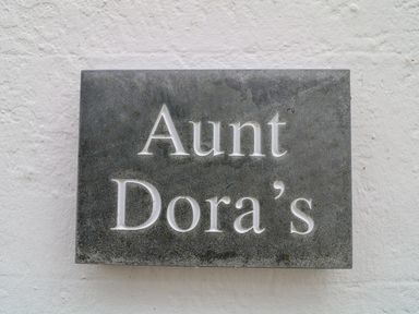 A gray stone plaque with the words Aunt Dora's on a white textured wall at Aunt Dora's in Port Isaac