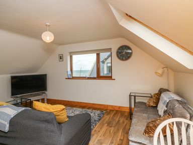 A living room with two sofas a television a wall clock and a window with a sea view at Old Field Hideaway Slade near Fethard-On-Sea County Wexford
