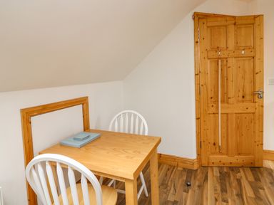 A wooden table with two white chairs a closed wooden door and wooden floor at Old Field Hideaway in Slade near Fethard-On-Sea County Wexford
