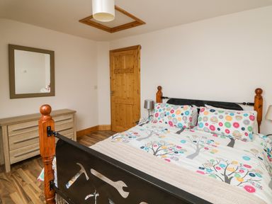 A bedroom with a bed with colorful bedding a wooden door a dresser with a mirror and wooden flooring at Old Field Hideaway in Slade near Fethard-On-Sea County Wexford