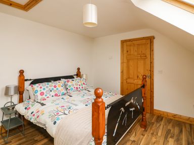 A bedroom with a wooden bed frame a patterned duvet a bedside table with a lamp and a wooden door at Old Field Hideaway Slade near Fethard-On-Sea County Wexford