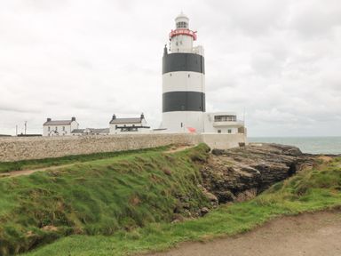 A lighthouse with black and white stripes near rocky coast and stone wall at Old Field Hideaway Slade near Fethard-On-Sea County Wexford