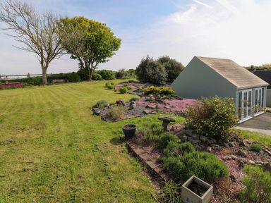 A garden with trimmed grass trees bushes and a small building at Tower Cottage Near Pembroke