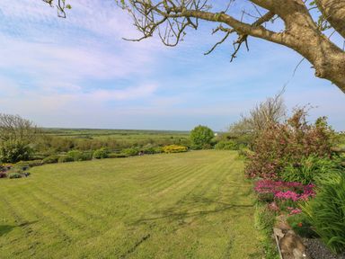 A large mowed lawn with flower beds and trees in a rural setting at Tower Cottage Near Pembroke