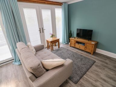 A living room with a sofa, small wooden tables, a TV on a wooden stand, and blue curtains at Tower Cottage Near Pembroke