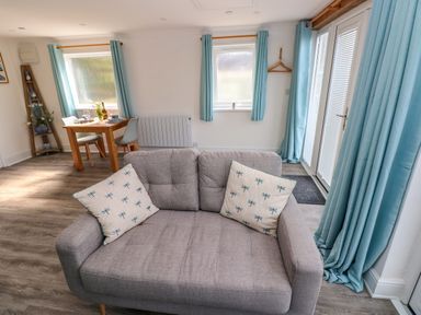 A living room with a gray sofa with patterned cushions a wooden dining table with two chairs and blue curtains at Tower Cottage Near Pembroke