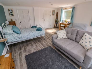 A room with a bed and sofa a small dining table with chairs and two closed doors at Tower Cottage Near Pembroke