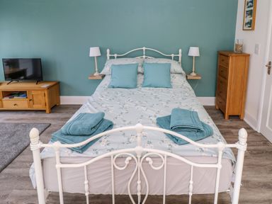 A bedroom with a bed with blue floral bedding and two blue towels on it a wooden cabinet and a wooden dresser near a blue wall at Tower Cottage Near Pembroke