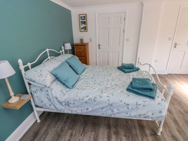 A bedroom with a white metal bed frame blue floral bedding folded towels on bed and wooden flooring at Tower Cottage Near Pembroke