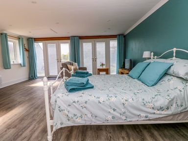 A bedroom with a white metal bed and floral bedspread next to blue curtains and wooden flooring at Tower Cottage Near Pembroke