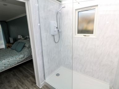 A shower with a glass door adjacent to a bedroom with a bed and bedside table at Tower Cottage Near Pembroke