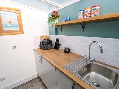 A kitchen countertop with a sink a knife block an air fryer a teapot a shelf with jars and a plant at Tower Cottage Near Pembroke