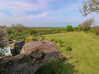 A garden with mowed grass shrubbery and trees with a view of fields at Tower Cottage Near Pembroke