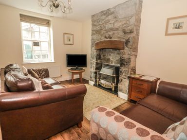 A living room with brown leather sofas a stone fireplace a small wooden table with a television and a window at Ty Potiwr Conwy