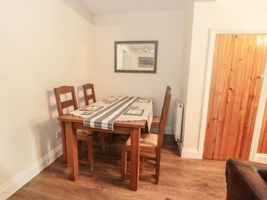 A dining area with a wooden table and four chairs a table runner and placemats on the table a mirror on the wall and a wooden door to the side at Ty Potiwr in Conwy