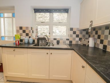 A kitchen countertop with a sink under a window and cabinets at Ty Potiwr in Conwy