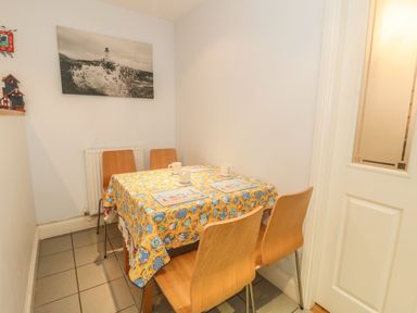 A small dining area with a table covered by a colorful tablecloth and four wooden chairs at Ty Potiwr in Conwy