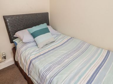 A single bed with striped bedding and two pillows in a small room at Ty Potiwr in Conwy