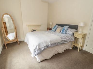 A bedroom with a double bed two bedside tables with lamps a standing mirror and a small fireplace at Ty Potiwr in Conwy