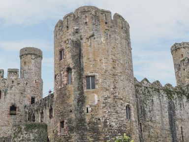 Stone medieval castle towers and walls with narrow windows under a cloudy sky