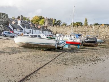 Boats on a sandy shore with a stone wall and houses in the background at Ty Potiwr in Conwy