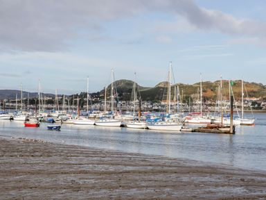 A harbor with sailboats docked on the water and hills with houses in the background at Ty Potiwr in Conwy