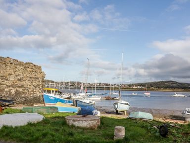 A shoreline with several boats on grass and water near a stone wall at Ty Potiwr in Conwy