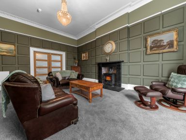 A living room with leather sofas a wooden coffee table a fireplace a clock on the wall and framed paintings at 8 Corkickle in Whitehaven