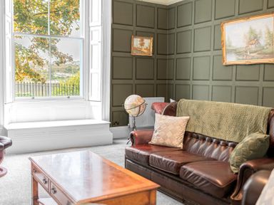 A sitting room with a leather sofa cushions coffee table globe and paintings on the wall at 8 Corkickle in Whitehaven