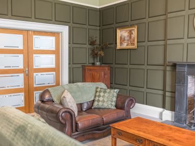 A living room with leather sofas wooden coffee table paneled walls and a small wooden cabinet at 8 Corkickle in Whitehaven