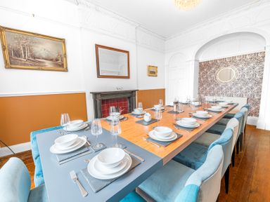A dining room with a long table set with white dishes and glasses surrounded by blue chairs at 8 Corkickle in Whitehaven