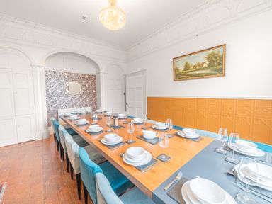A dining room with a long wooden table set with white dishes and blue chairs at 8 Corkickle in Whitehaven