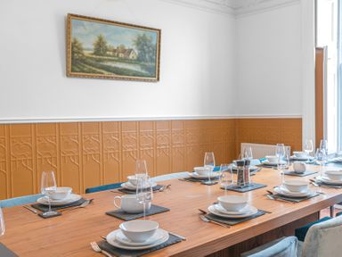 A dining room with a wooden table set with white dishes and glasses and a painting on the wall at 8 Corkickle in Whitehaven