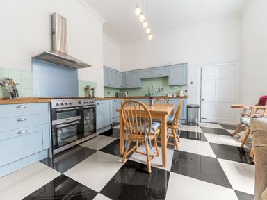 A kitchen with light blue cabinets wooden table and chairs and black and white checkered floor at 8 Corkickle in Whitehaven