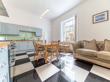 A kitchen with blue cabinets a wooden dining table with chairs a beige sofa and a large window at 8 Corkickle in Whitehaven