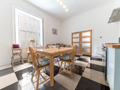 A dining area with a wooden table and six chairs on a black and white checkered floor at 8 Corkickle in Whitehaven