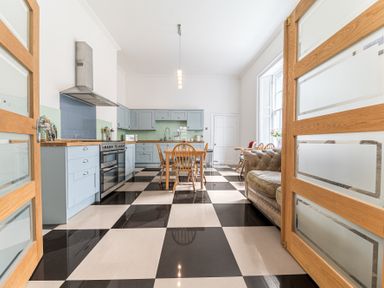 A kitchen with a black and white checkered floor wooden dining table light blue cabinets and a brown sofa at 8 Corkickle in Whitehaven